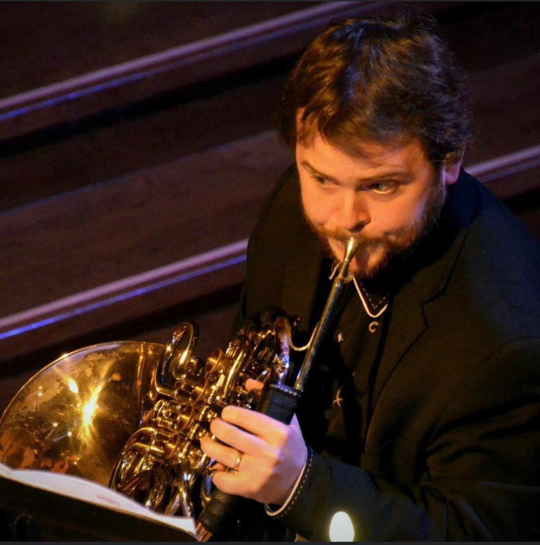 Jason DeWater playing French horn on stage